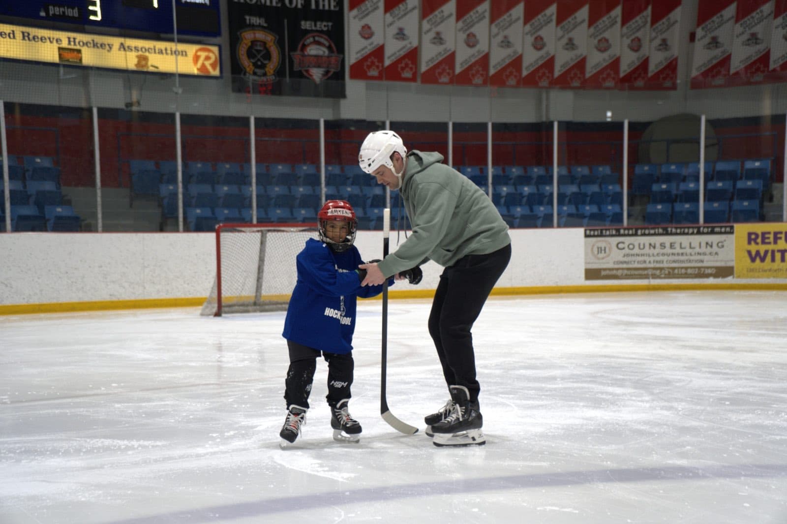 A coach leans in to help a young skater on the ice